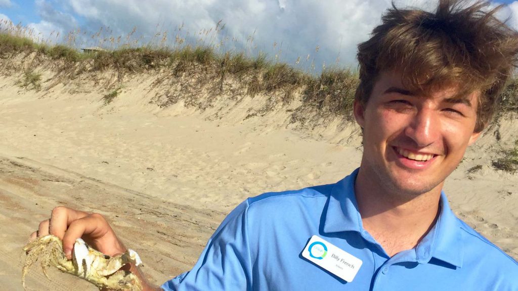 a student intern holding a crab on the beach